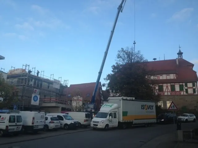 Lieferfahrzeug und Autokran vor einem Fachwerkhaus in einer Ortsmitte