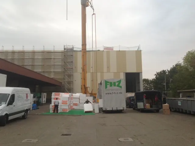 FHZ-Lieferfahrzeug vor einem eingerüsteten Rohbau, daneben ein Baukran
