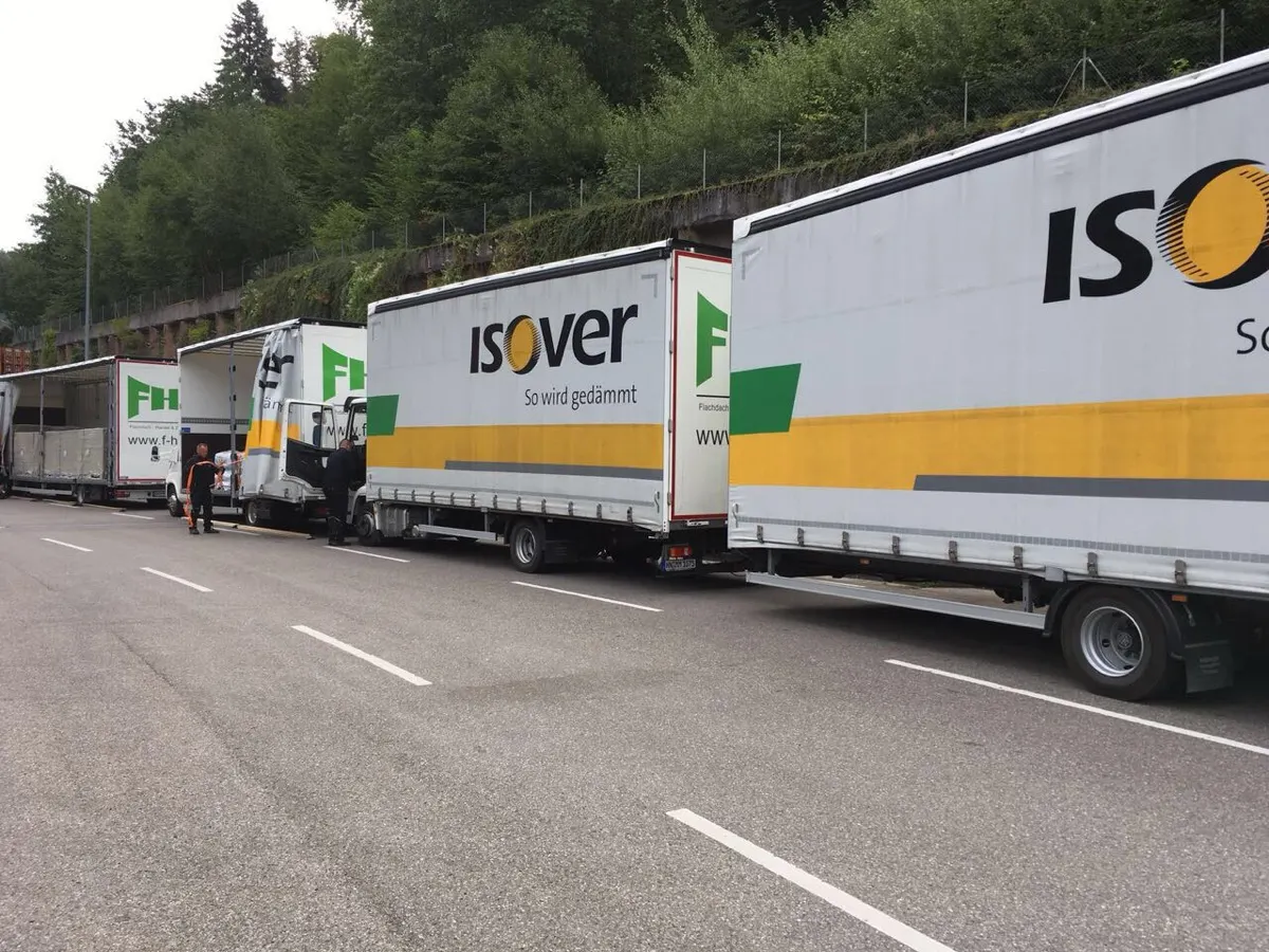 Mehrere Lkw mit Isover-Ladung stehen hintereinander an einer Straße